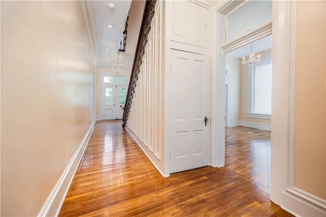 hallway with hardwood / wood-style flooring, crown molding, and a chandelier