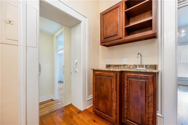 bar with hardwood / wood-style flooring, sink, and light stone counters