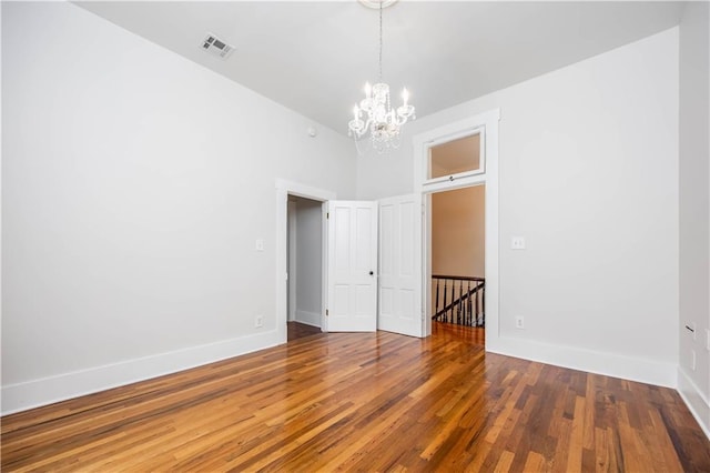 spare room with an inviting chandelier and hardwood / wood-style flooring