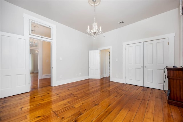 unfurnished bedroom featuring an inviting chandelier, wood-type flooring, and a closet