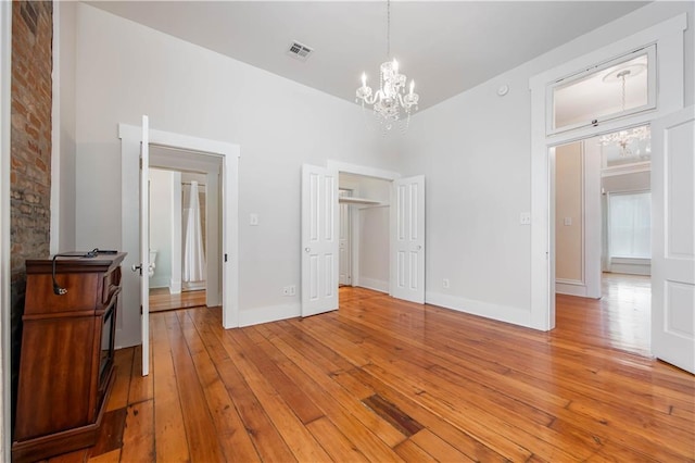 unfurnished bedroom with a towering ceiling, a notable chandelier, a closet, and light wood-type flooring