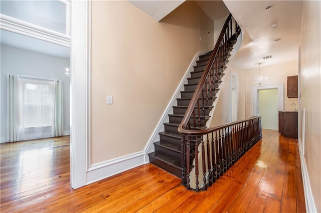 stairs with hardwood / wood-style floors and a notable chandelier