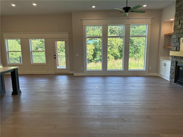 unfurnished living room featuring ceiling fan, a stone fireplace, dark wood-type flooring, and a healthy amount of sunlight