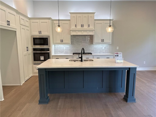 kitchen with appliances with stainless steel finishes, hanging light fixtures, decorative backsplash, light stone counters, and dark hardwood / wood-style flooring