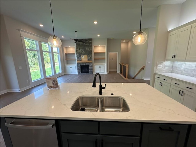 kitchen featuring light stone counters, ceiling fan, sink, a stone fireplace, and a center island with sink