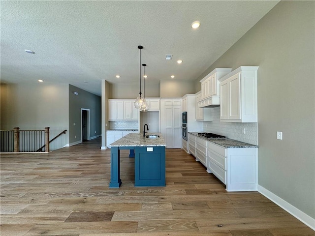 kitchen with pendant lighting, a kitchen island with sink, stainless steel gas stovetop, and white cabinetry