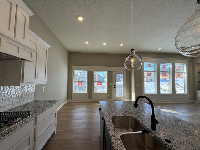 kitchen with dark wood finished floors, stainless steel appliances, white cabinetry, a sink, and light stone countertops