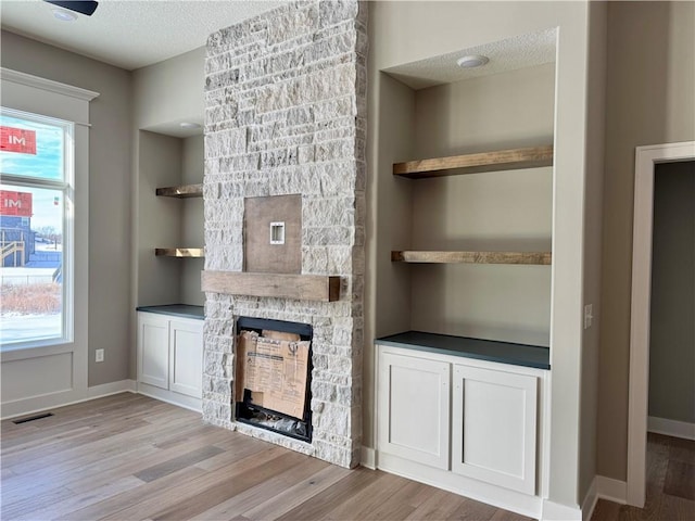 unfurnished living room featuring light wood-style floors, visible vents, a textured ceiling, and built in features