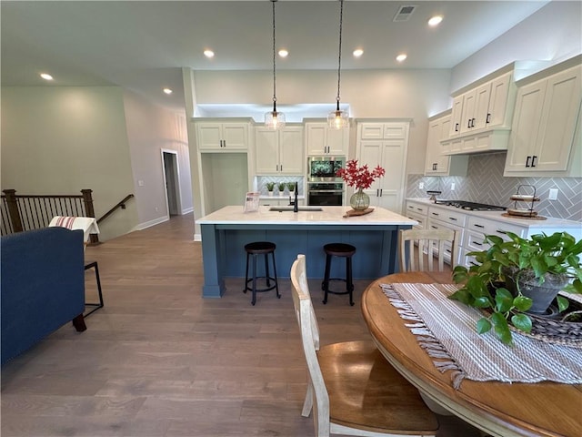 kitchen with appliances with stainless steel finishes, an island with sink, hardwood / wood-style flooring, a breakfast bar area, and decorative light fixtures