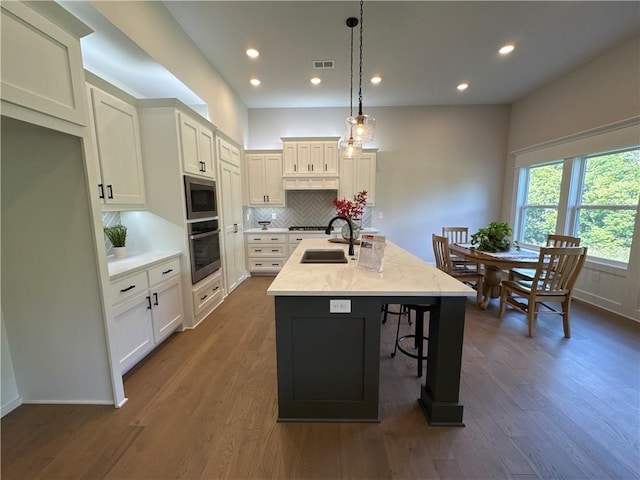 kitchen featuring dark hardwood / wood-style flooring, stainless steel appliances, sink, pendant lighting, and a center island with sink