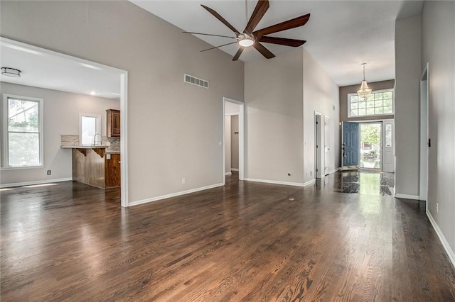 unfurnished living room featuring a towering ceiling, dark hardwood / wood-style floors, a wealth of natural light, and ceiling fan