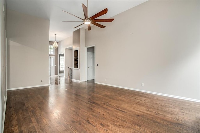 unfurnished living room with ceiling fan, a towering ceiling, and dark hardwood / wood-style floors