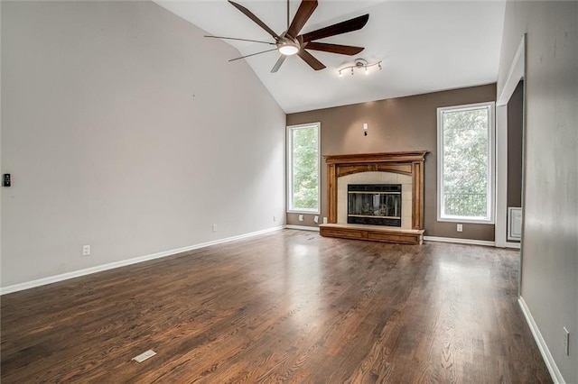 unfurnished living room featuring a tiled fireplace, a wealth of natural light, dark wood-type flooring, and lofted ceiling