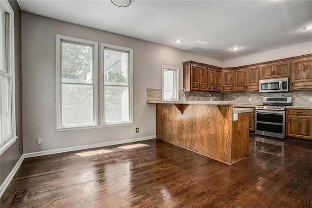 kitchen with kitchen peninsula, tasteful backsplash, a wealth of natural light, stainless steel appliances, and a breakfast bar area