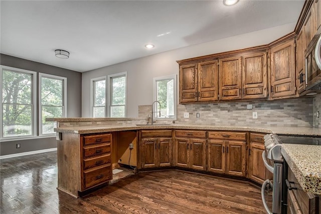 kitchen featuring light stone countertops, backsplash, stainless steel stove, and sink