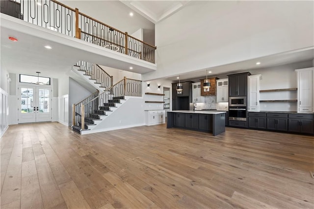 kitchen featuring wood-type flooring, appliances with stainless steel finishes, a towering ceiling, and an island with sink