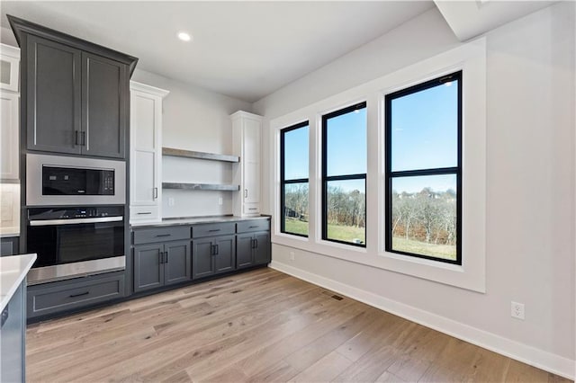 kitchen featuring built in microwave, stainless steel oven, white cabinets, and light hardwood / wood-style floors