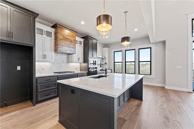 kitchen featuring backsplash, a kitchen island with sink, pendant lighting, light hardwood / wood-style flooring, and white cabinets