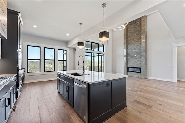 kitchen featuring dishwasher, sink, light hardwood / wood-style floors, decorative light fixtures, and a center island with sink