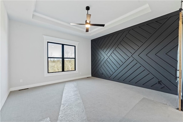 unfurnished room with a barn door, light colored carpet, a raised ceiling, and ceiling fan