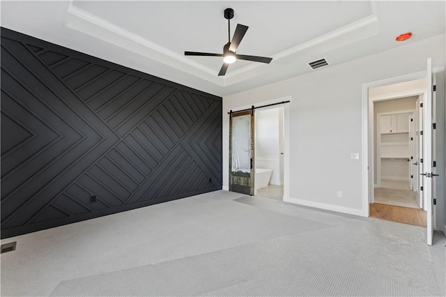 unfurnished bedroom featuring a raised ceiling, a barn door, and ceiling fan