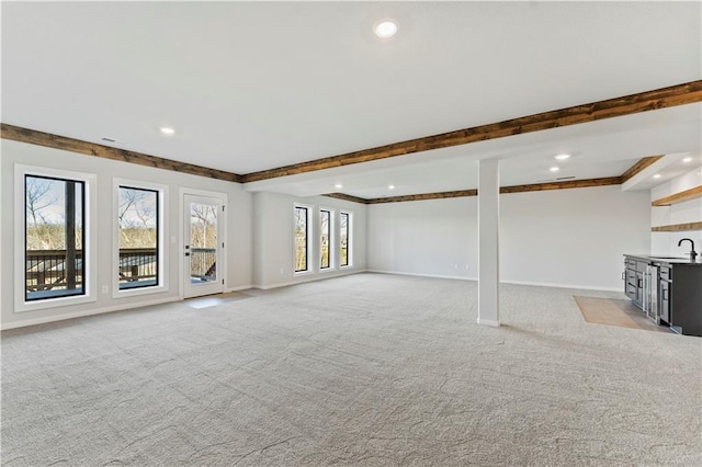 unfurnished living room featuring crown molding, light carpet, sink, and a healthy amount of sunlight