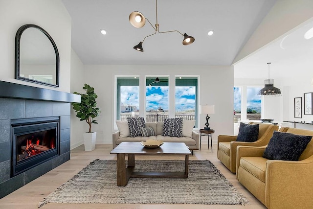 living room with a tiled fireplace, vaulted ceiling, and light hardwood / wood-style floors