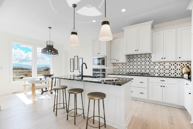 kitchen with sink, hanging light fixtures, an island with sink, and white cabinets