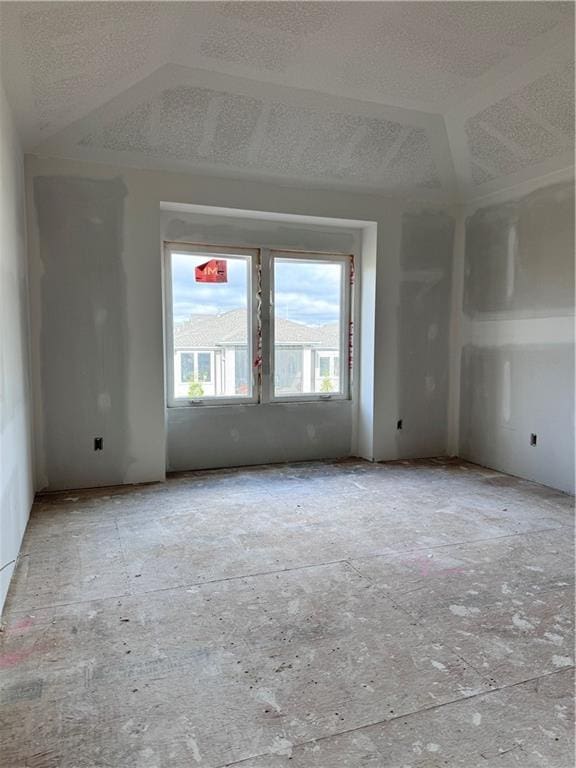 unfurnished room featuring vaulted ceiling and a textured ceiling