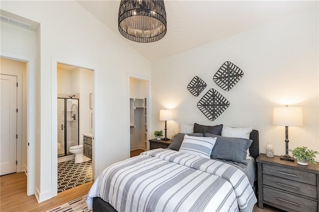 bedroom with light wood-type flooring, a walk in closet, vaulted ceiling, connected bathroom, and a closet