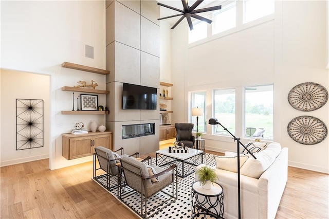 living room featuring a tile fireplace, a high ceiling, and light hardwood / wood-style flooring