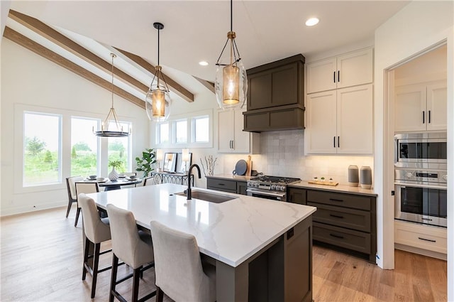 kitchen with sink, stainless steel appliances, vaulted ceiling with beams, a center island with sink, and white cabinets