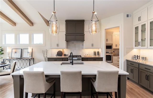 kitchen with beamed ceiling, decorative light fixtures, white cabinets, and a kitchen island with sink