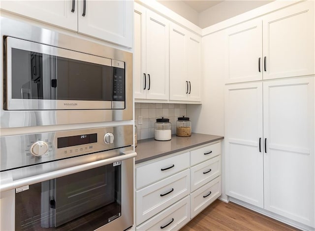 kitchen with decorative backsplash, light wood-type flooring, white cabinetry, and appliances with stainless steel finishes