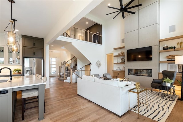 living room featuring a fireplace, ceiling fan, light wood-type flooring, and sink