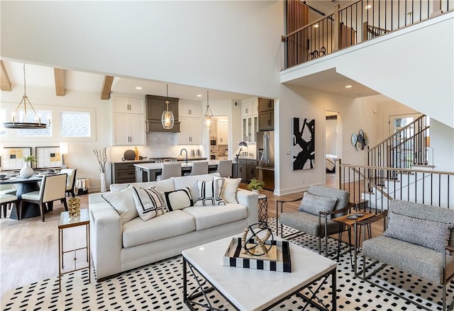 living room with a chandelier, beam ceiling, a high ceiling, and light hardwood / wood-style flooring