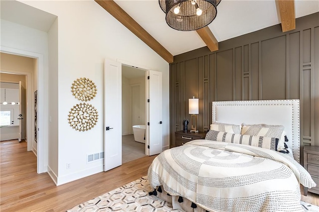 bedroom with vaulted ceiling with beams, light hardwood / wood-style floors, a chandelier, and ensuite bath