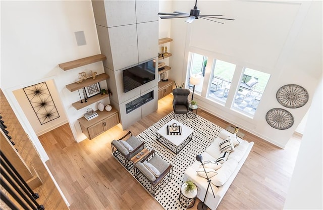 living room featuring a high ceiling, light wood-type flooring, and ceiling fan