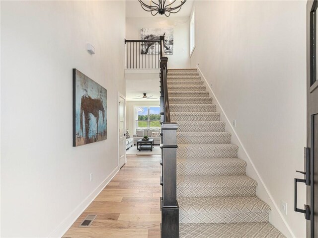 stairs with ceiling fan with notable chandelier and hardwood / wood-style flooring