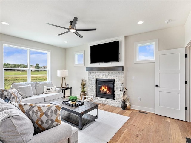 living room with ceiling fan, a stone fireplace, and light hardwood / wood-style flooring