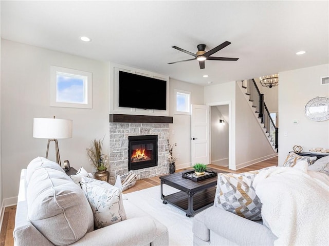 living room with a stone fireplace, ceiling fan with notable chandelier, and light hardwood / wood-style flooring