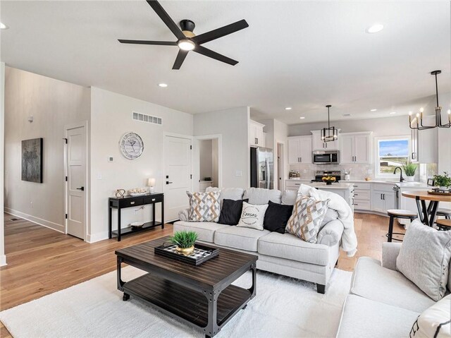 living room with light hardwood / wood-style floors, ceiling fan with notable chandelier, and sink