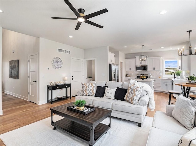 living room with sink, ceiling fan with notable chandelier, and light wood-type flooring