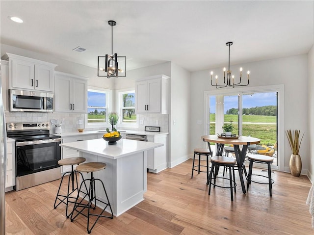 kitchen featuring white cabinets, appliances with stainless steel finishes, a center island, and an inviting chandelier