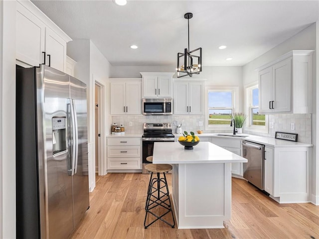 kitchen with a kitchen island, white cabinetry, stainless steel appliances, sink, and hanging light fixtures