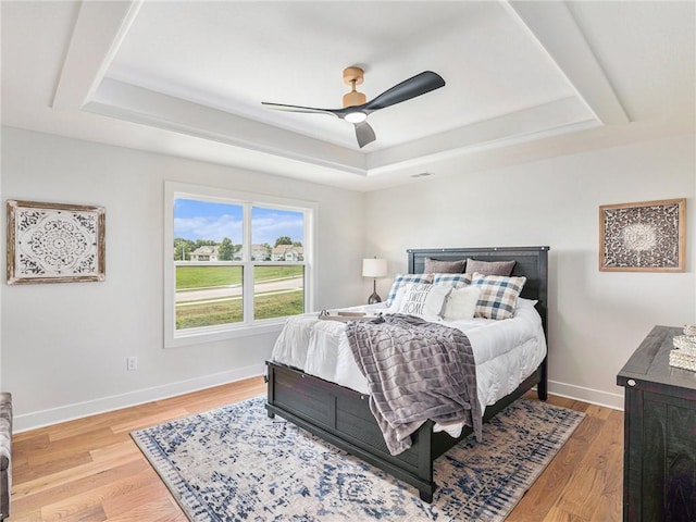 bedroom with ceiling fan, a tray ceiling, and light wood-type flooring