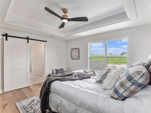 bedroom with a raised ceiling, a barn door, ceiling fan, and light hardwood / wood-style floors