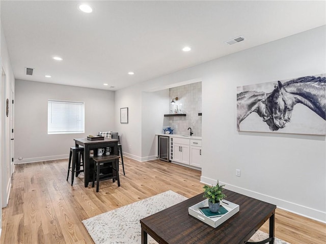 dining area featuring indoor wet bar, beverage cooler, and light hardwood / wood-style flooring