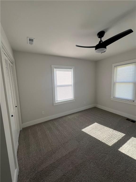 empty room featuring a wealth of natural light, ceiling fan, and dark carpet