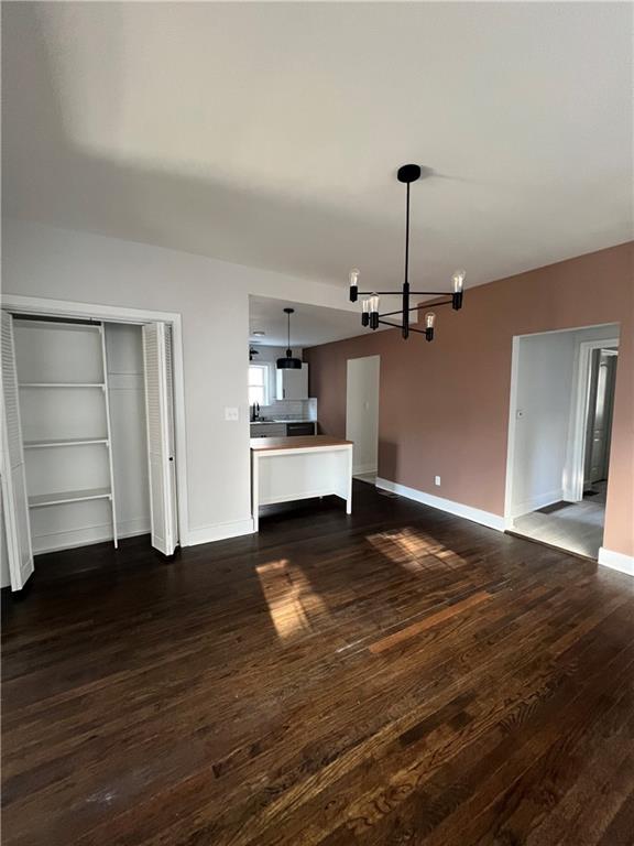 unfurnished living room featuring a notable chandelier and dark wood-type flooring